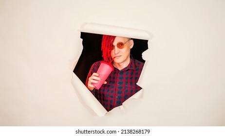 Young man in red plaid shirt drinking through soft drink straw in hole of white background. Bright guy enjoying nonalcoholic beverage. - Shutterstock ID 2138268179
