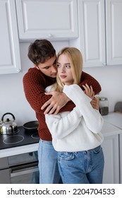 Young Man In Red Sweater Hugging Blonde Girlfriend In Kitchen