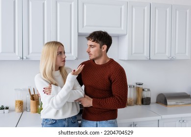 Young Man In Red Sweater Looking At Blonde Girlfriend In Kitchen