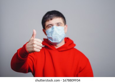 Young Man In Red Sweatshirt Wearing A Protective Mask On His Face And Showing A Finger Up, Concept Health, Gesture Optimistic Outlook In Future, Survivor Behavior