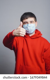 Young Man In Red Sweatshirt Wearing A Protective Mask On His Face And Showing A Finger Up, Concept Health, Gesture Optimistic Outlook In Future, Survivor Behavior