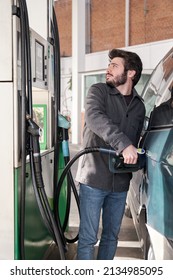 Young Man Refueling His Vehicle With Gasoline While Looking At The Prices At A Gas Station.