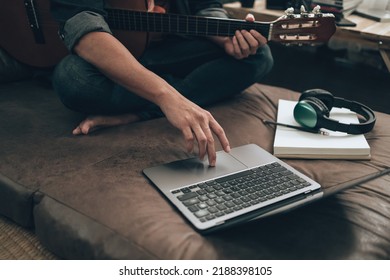 young man relax and playing guitar while sitting on sofa bed in living room at home. Music create melody song, lyrics on laptop and practice concept. - Shutterstock ID 2188398105