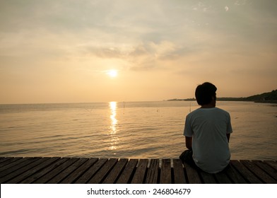 Young man relax siting on sea beach pier looks to right with sunset sky. Conceptual for thinking and looking for concentrate somethings in Summer background with copy space label text banner.