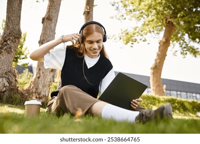 A young man relaxes outdoors, listening to music, and working on a laptop on a sunny day. - Powered by Shutterstock