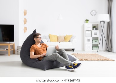 Young man relaxing comfortably in a grey sitting sack in a bright studio flat