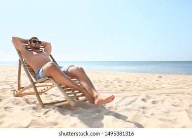 Young Man Relaxing In Deck Chair On Sandy Beach