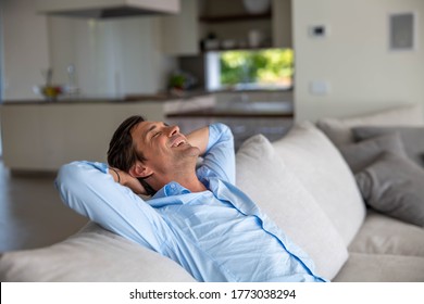 An young man is relaxing and enjoying rest by leaning on soft comfortable sofa in living room at home.
