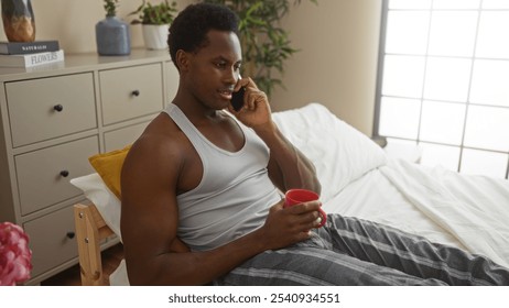 Young man relaxing indoors on a bed with a red mug while talking on the phone in a cozy bedroom setting - Powered by Shutterstock