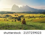 Young man relaxing on alpine meadow in Dolomites Alp mountains Seiser Alm or Alpe di Siusi at sunrise. Trentino Alto Adige or South Tyrol, Italy. Focus on the guy on foreground