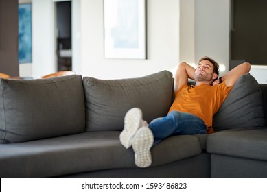 Young man relaxing on his living room sofa with his eyes closed and hands behind his head  - Powered by Shutterstock