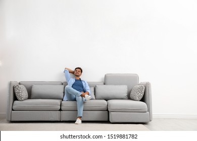Young man relaxing on sofa against white wall