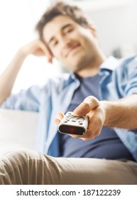 Young Man Relaxing On Sofa And Holding TV Remote Control.