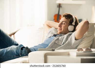 Young man relaxing on sofa with headphones in the living room. - Powered by Shutterstock