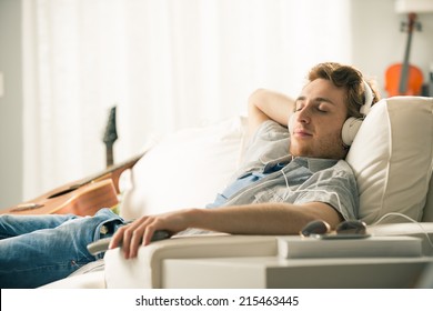 Young man relaxing on sofa with headphones in the living room.