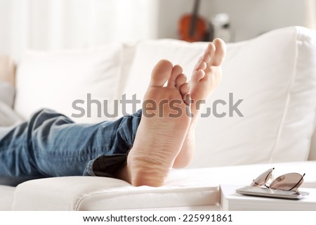 Young man relaxing on sofa in the living room, feet close-up.
