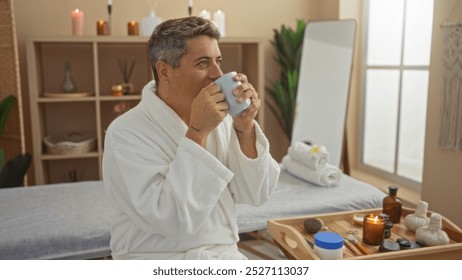 Young man relaxing in a spa room sipping tea, surrounded by wellness items on a wooden tray and candles in a serene setting - Powered by Shutterstock