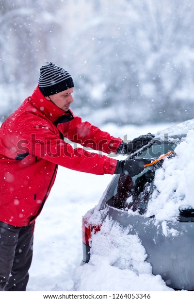 young man removing snow from car. Man
cleaning snow from car windshield with brush, close up. Snowy
winter weather. Car in snow after snowstorm.

