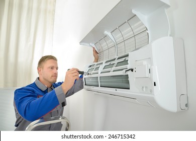 Young Man Repairing Air Conditioner Standing On Stepladder