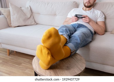 Young man resting, lying on sofa and playing video games.