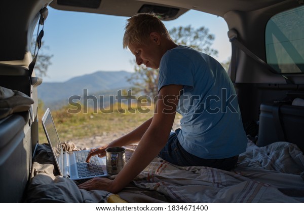 Young man resting in nature with an off-road\
vehicle resting in the trunk of a car. Uses a laptop for\
communication and Internet\
access