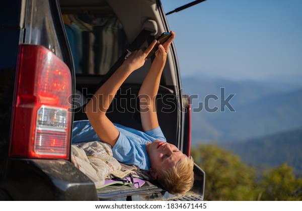 Young man resting in\
nature with an off-road vehicle resting in the trunk of a car.\
Communicates on a mobile phone using cellular communication and the\
Internet.