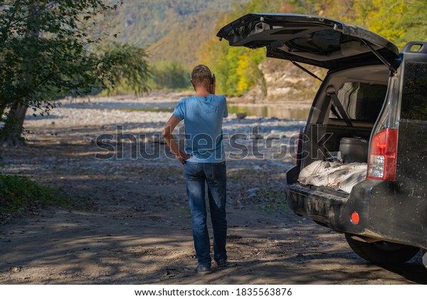 Young man resting in\
nature with an off-road vehicle resting in the trunk of a car.\
Communicates on a mobile phone using cellular communication and the\
Internet.