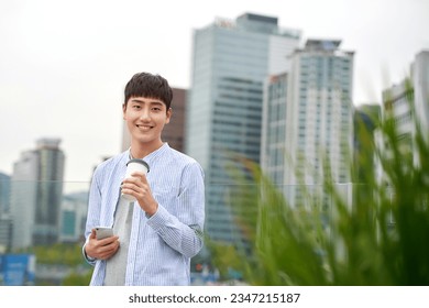 A young man is resting on a land bridge with coffee and a smartphone in the background of a busy street during the day. - Powered by Shutterstock