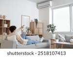 Young man resting on sofa in room with operating air conditioner