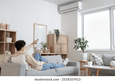 Young man resting on sofa in room with operating air conditioner