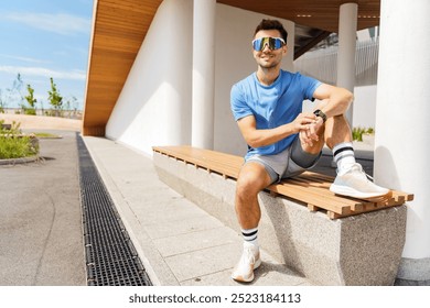 Young Man Resting on a Wooden Bench in a Modern Outdoor Space While Wearing Sporty Attire and Sunglasses on a Sunny Day - Powered by Shutterstock