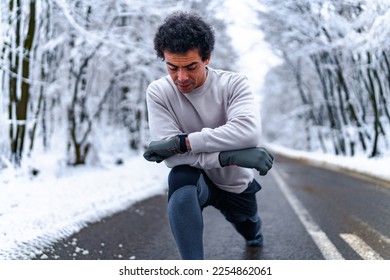 Young man resting and stretching after running in mountain road on cold winter day. - Shutterstock ID 2254862061