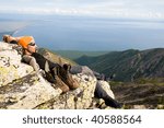 young man rests on stone having climbed up mountain top