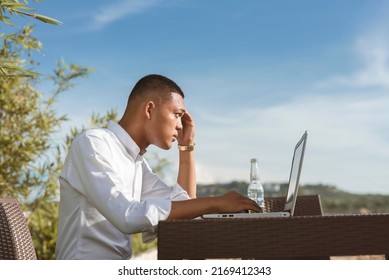 A Young Man Reviewing Data On His Laptop While Having A Bottle Of Beer At An Outdoor Cafe With Great Scenery.