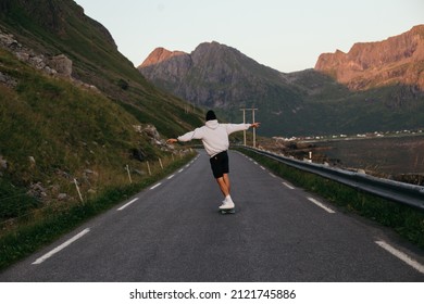 Young man ride on longboard on empty mountain road. Millennial freedom and outdoor vibes lifestyle. Skateboarding culture