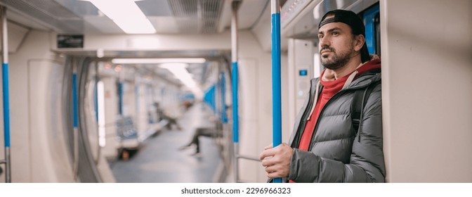 A young man rides standing in a modern subway car. A handsome Caucasian guy in a jacket stands after a working day in a half-empty subway car on the daily way home - Powered by Shutterstock