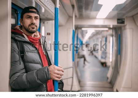 A young man rides standing in a modern subway car. A handsome Caucasian guy in a jacket stands after a working day in a half-empty subway car on the daily way home