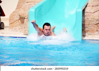 Young Man Riding Down A Yellow Water Slide .Man Enjoying A Water Tube Ride