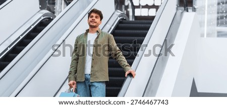 Young Man Riding Escalator While Holding Shopping Bags in a Mall During Daytime