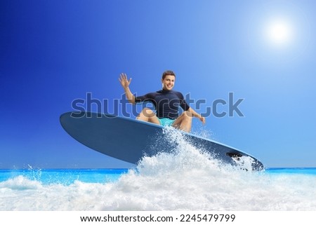 Young man riding a surfboard in the sea and smiling at camera