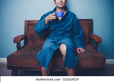 Young Man In Robe Drinking Coffee On Sofa