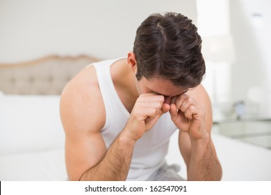 Young Man Rubbing His Eyes In Bed At Home