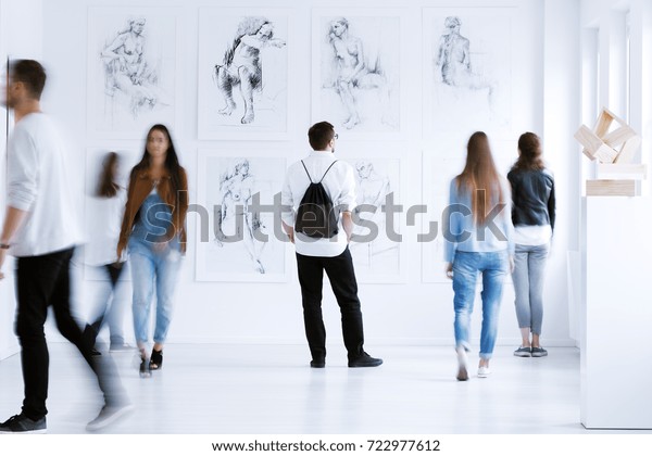 Young man with rucksack on back visiting art\
gallery with drawings and\
sculpture