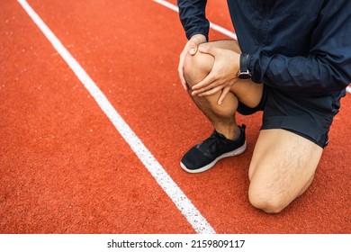 Young Man Runner Has Sore Knee Because He Ran Too Long. Male Exercising Until The Injury. Overtrained. Young Sport Man Accident Running On Track