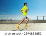 Young man running along a waterfront promenade on a sunny day in vibrant athletic gear