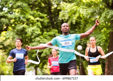 Young Man Running In The Crowd Crossing The Finish Line.