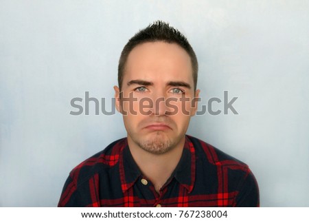A young man with a sad expression. Frustrated guy. Portrait of a sad man. Portrait of young modern trendy guy against a blue background. Man cry with tears.