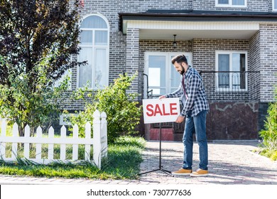 young man with sale board selling his house - Shutterstock ID 730777636