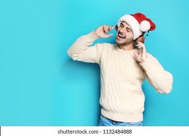 Young Man In Santa Hat Listening To Christmas Music On Color Background