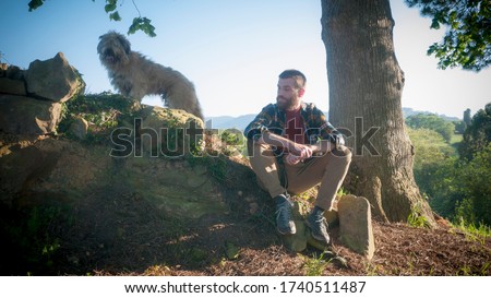 Young man sat under a tree with dog in country side
